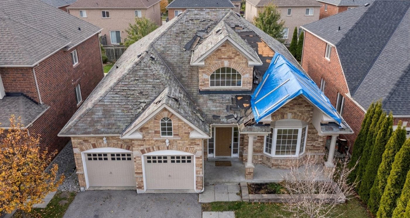 Storm-damaged roof with missing shingles and emergency tarp